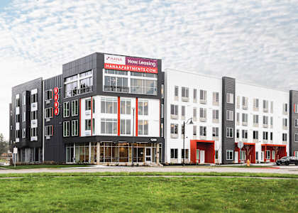 A modern building with a red and white sign that says "Hana Now Leasing".