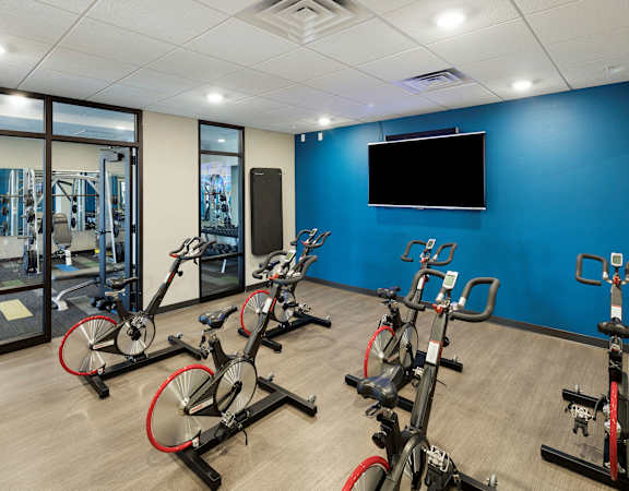 A gym with a row of stationary bikes and a television on the wall.