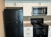 Thumbnail 35 of 48 - A black fridge in a kitchen with a white oven and microwave.