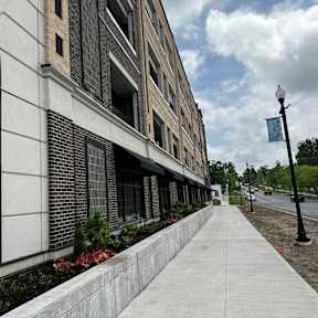 A sidewalk runs alongside a building with a brick facade and a street lamp.