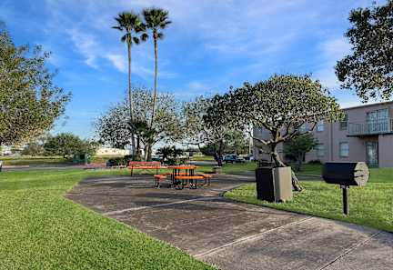 A park with a picnic table and bench in front of a building.