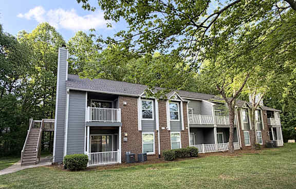 Apartment building with a grey and brown exterior and a tree in front.