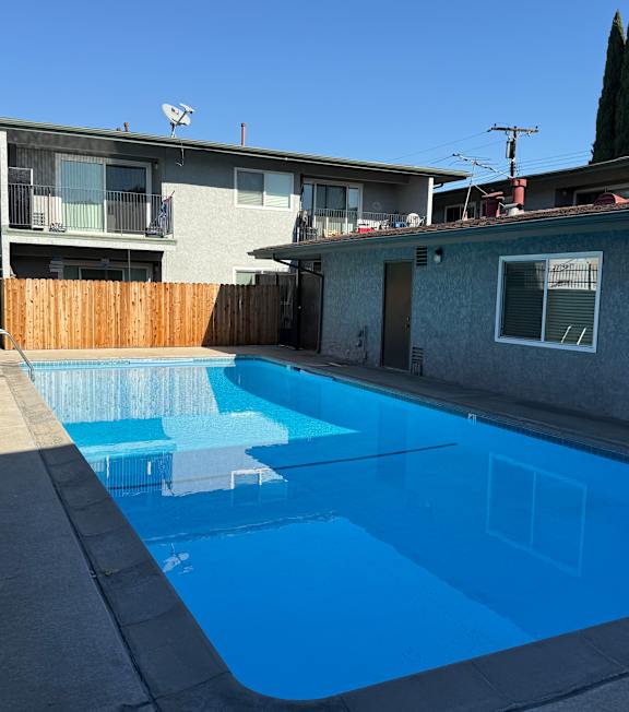 A pool with a hot tub and lounge chairs in front of a building.