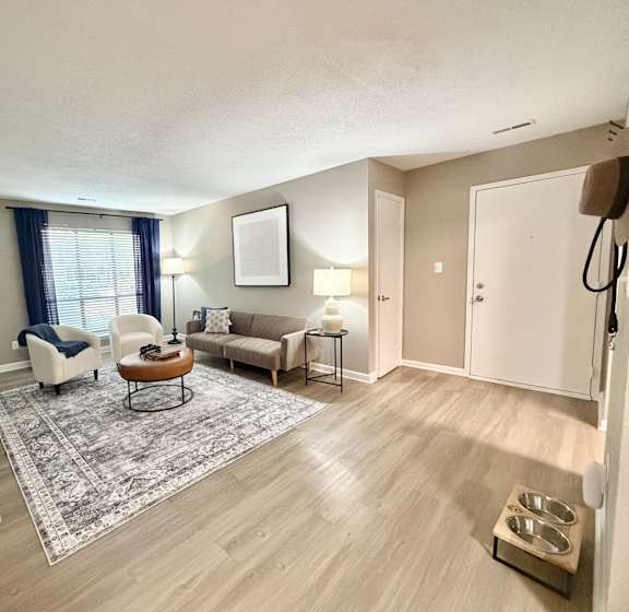 A living room with a white chair, a brown coffee table, a beige couch, and a grey rug.