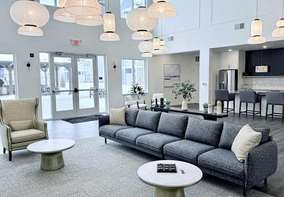 A grey couch with a white pillow is in the middle of a room with a grey carpet.