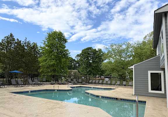 A pool surrounded by trees and chairs.