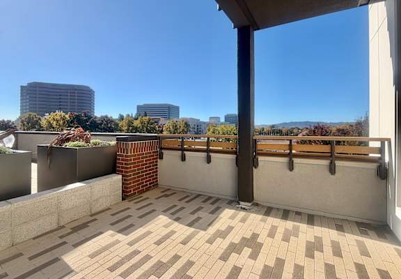 A balcony with a brick pillar and tiled floor overlooks a cityscape.
