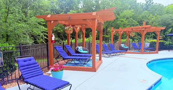 A poolside area with blue lounge chairs and a wooden pergola.