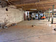 A man is standing in a large, empty warehouse with a forklift in the background.