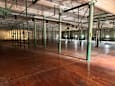 A large empty warehouse with wooden floors and green pillars.