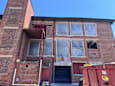 A building with a red door and windows covered in plastic.