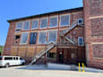 A white van is parked in front of a brick building with a staircase leading to the entrance.