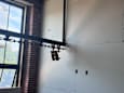 A white wall with a black pipe and three lights on it.
