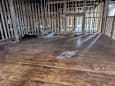 A room under construction with wooden flooring and exposed wall studs.