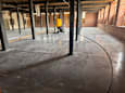 A yellow and black floor cleaning machine is in the middle of a large, empty room with concrete floors and brick walls.