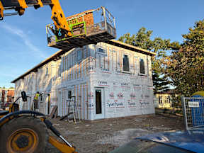 A construction site with a building under construction covered in insulation and a crane is in the foreground.