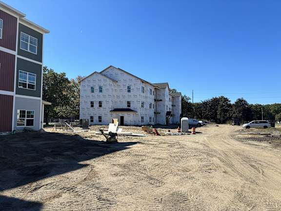 A construction site with a partially built white house and a red building to the left.