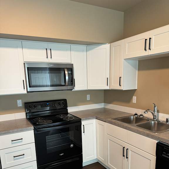 A modern kitchen with black and white appliances and wooden flooring.