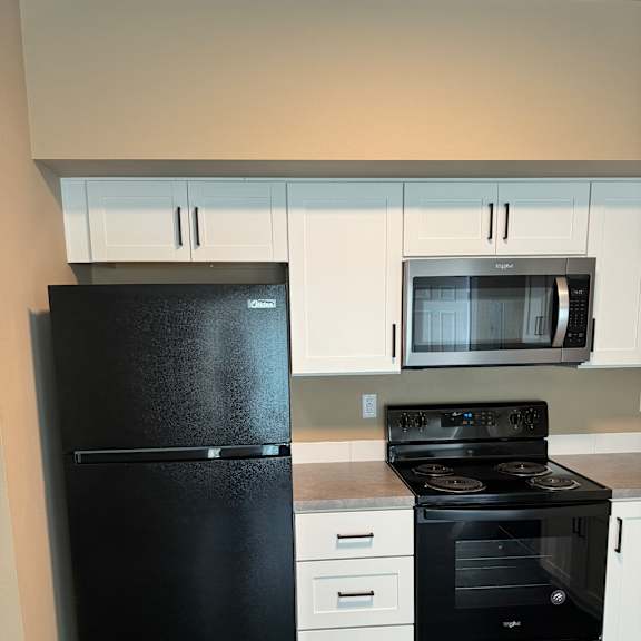 A black fridge in a kitchen with a white oven and microwave.