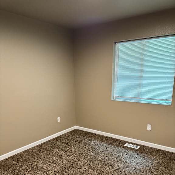 A room with a window and a brown carpet.