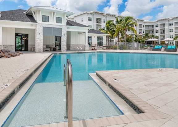 A large pool surrounded by white lounge chairs and palm trees.