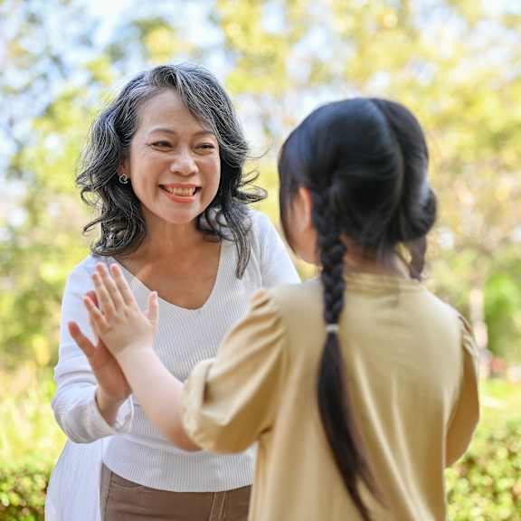 A woman and a girl are standing outside with trees in the background.