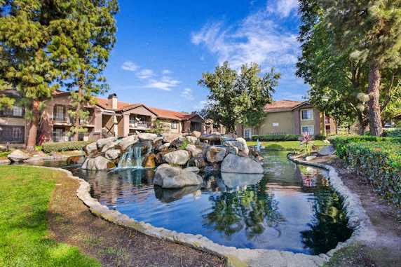 a fountain in the middle of pond surrounded by a grassy area with apartment homes in the background  at Citrine Hills, Ontario, CA, 91761