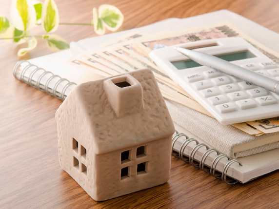 A small house model sits on a notebook next to a calculator and some money.