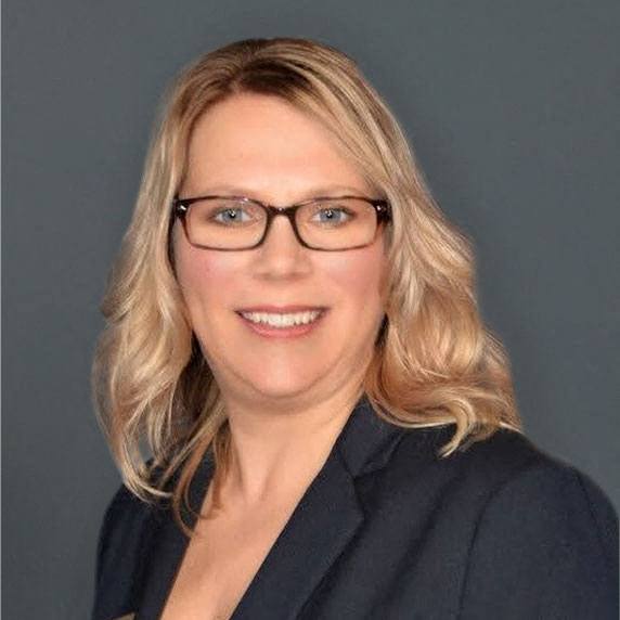 A woman with blonde hair and glasses wearing a dark blue blazer.