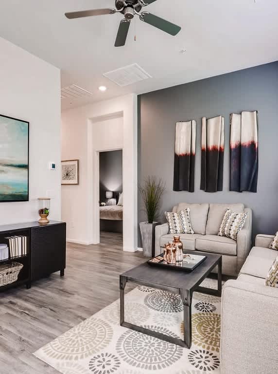 A living room with a grey couch, a coffee table, and a painting on the wall at Avilla Lehi Crossing, Mesa