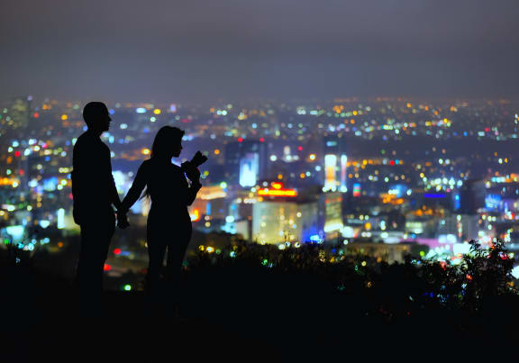 a man and woman look out over a cityscape at night