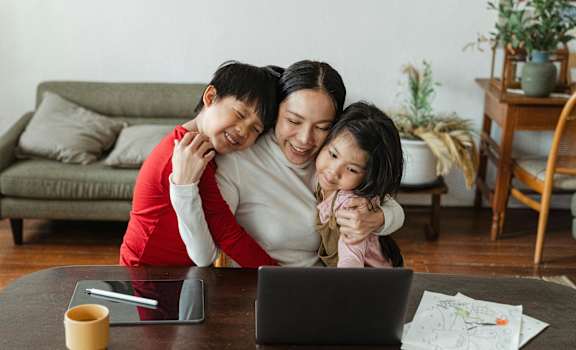 A family of three is sitting together at a table with a laptop and a tablet.