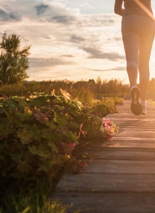a woman walking down a wooden path at sunset