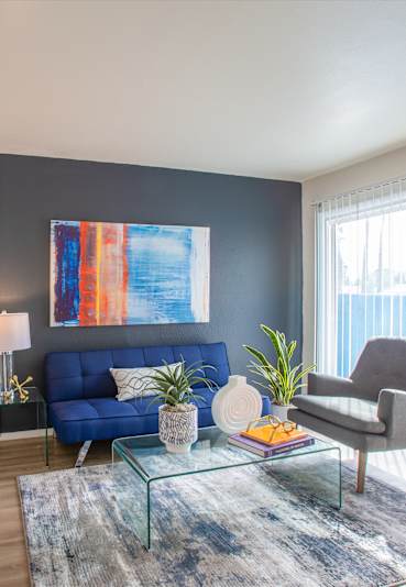 A living room with a blue couch and a large painting on the wall.