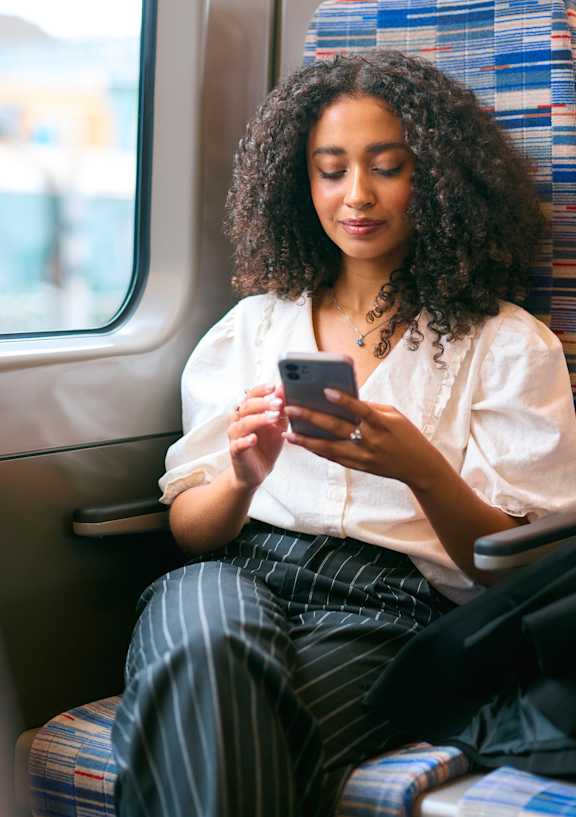 A woman with curly hair is sitting on a train, looking at her phone.
