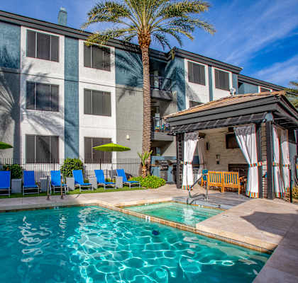 A pool area with a building in the background and a palm tree in the foreground.