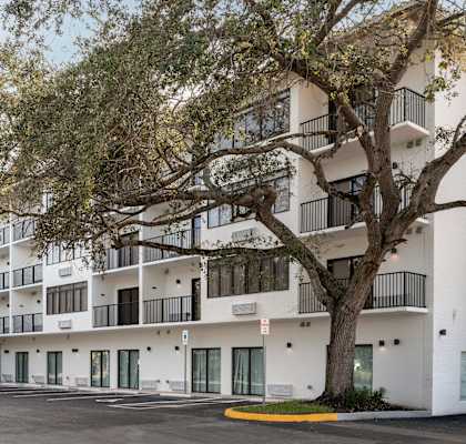 A large white building with balconies and a tree in front.