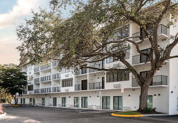 A large white building with balconies and a tree in front.