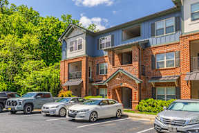A row of cars parked in front of a two-story apartment building.