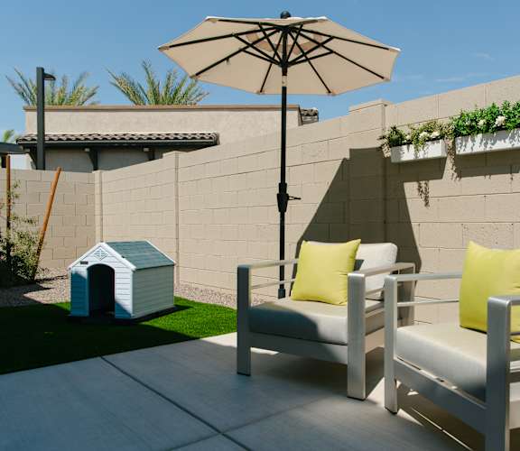 A patio with a white chair and a white umbrella.