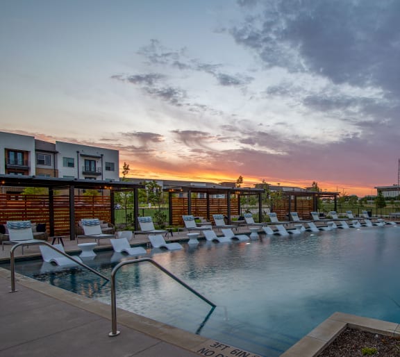 a swimming pool with chairs and umbrellas at sunset