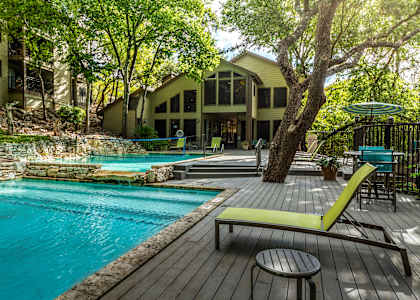 A wooden deck with a green chair and a small table is in front of a pool.