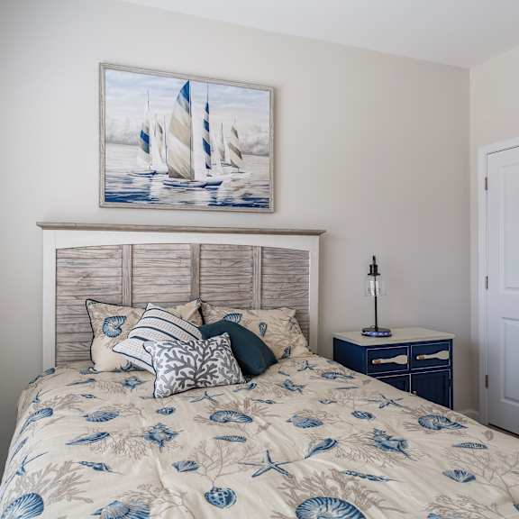 A bedroom with a bed, nightstand, and a painting of sailboats on the wall at Stepping Stone at Bridgewater Apartments, South Carolina