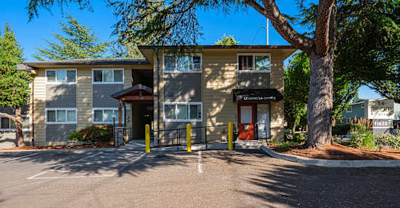 the front of a building with a parking lot and a tree