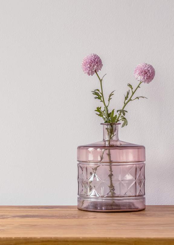 A glass jar with flowers in it is on a wooden surface.