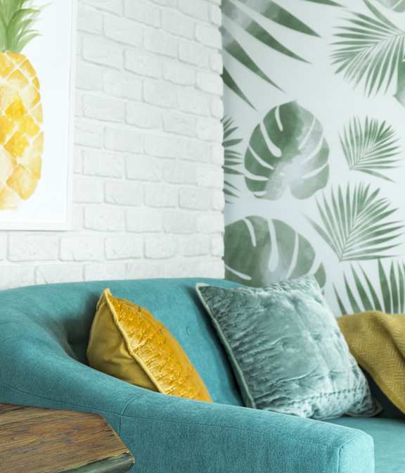 A living room with a blue couch, a pineapple print on the wall, and a wooden table with plants and candles.