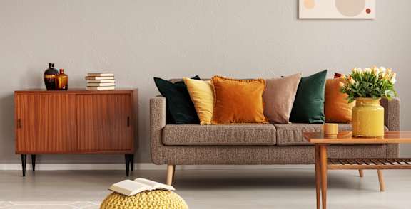 A living room with a grey couch, a wooden cabinet, a yellow stool, and a painting on the wall.