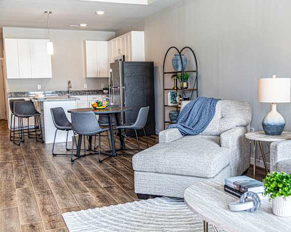 A modern living room with a grey couch, a white coffee table, and a kitchen area in the background.