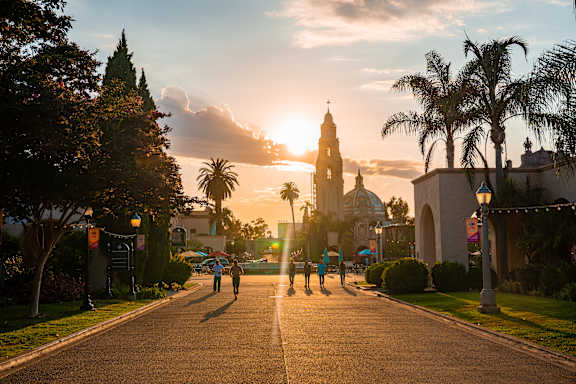 A street with people walking and a sunset in the background.