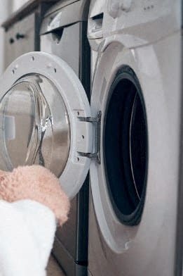 a person putting a pink towel into a washing machine